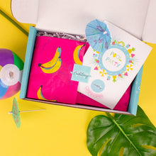 Load image into Gallery viewer, Open box containing party supplies with a pink notebook, colorful cards, and decorative items on a yellow background.