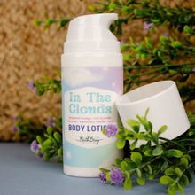Load image into Gallery viewer, Body lotion bottle labeled &#39;In The Clouds&#39; with greenery and flowers in the background