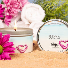 Load image into Gallery viewer, Candle with &#39;Aloha&#39; label surrounded by pink flowers and towels on sand