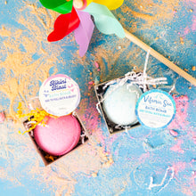 Load image into Gallery viewer, Two bath bombs in boxes with colorful labels on a textured blue background.