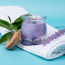 Load image into Gallery viewer, Purple candle in a glass jar with a wooden lid, surrounded by lavender flowers and green leaves on a blue background.