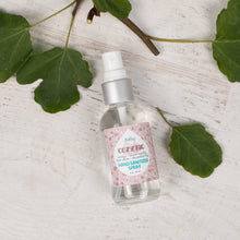 Load image into Gallery viewer, Hand sanitizer spray bottle with a pink label on a light wooden surface with green leaves.