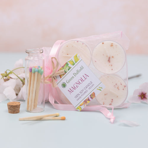 A set of handmade soy wax tealight candles with visible floral inclusions, presented in a clear packaging with a pink ribbon, accompanied by matches and a cork stopper.