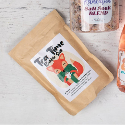 Collection of bath and body products on a light wooden surface with a 'Let's get cozy' card.